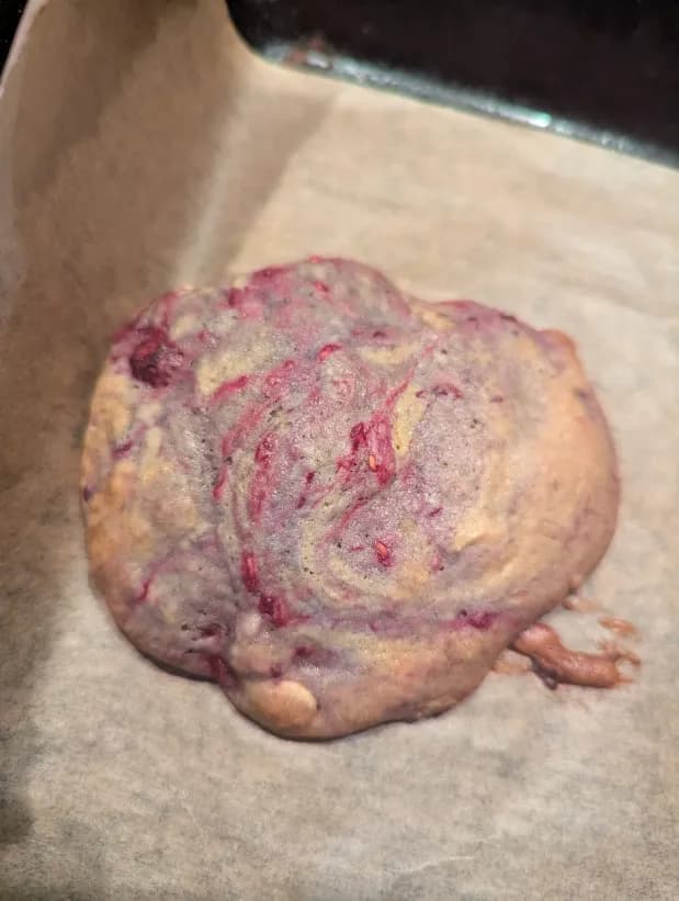 top-down photograph of a raspberry and white chocolate cookie in a baking tray